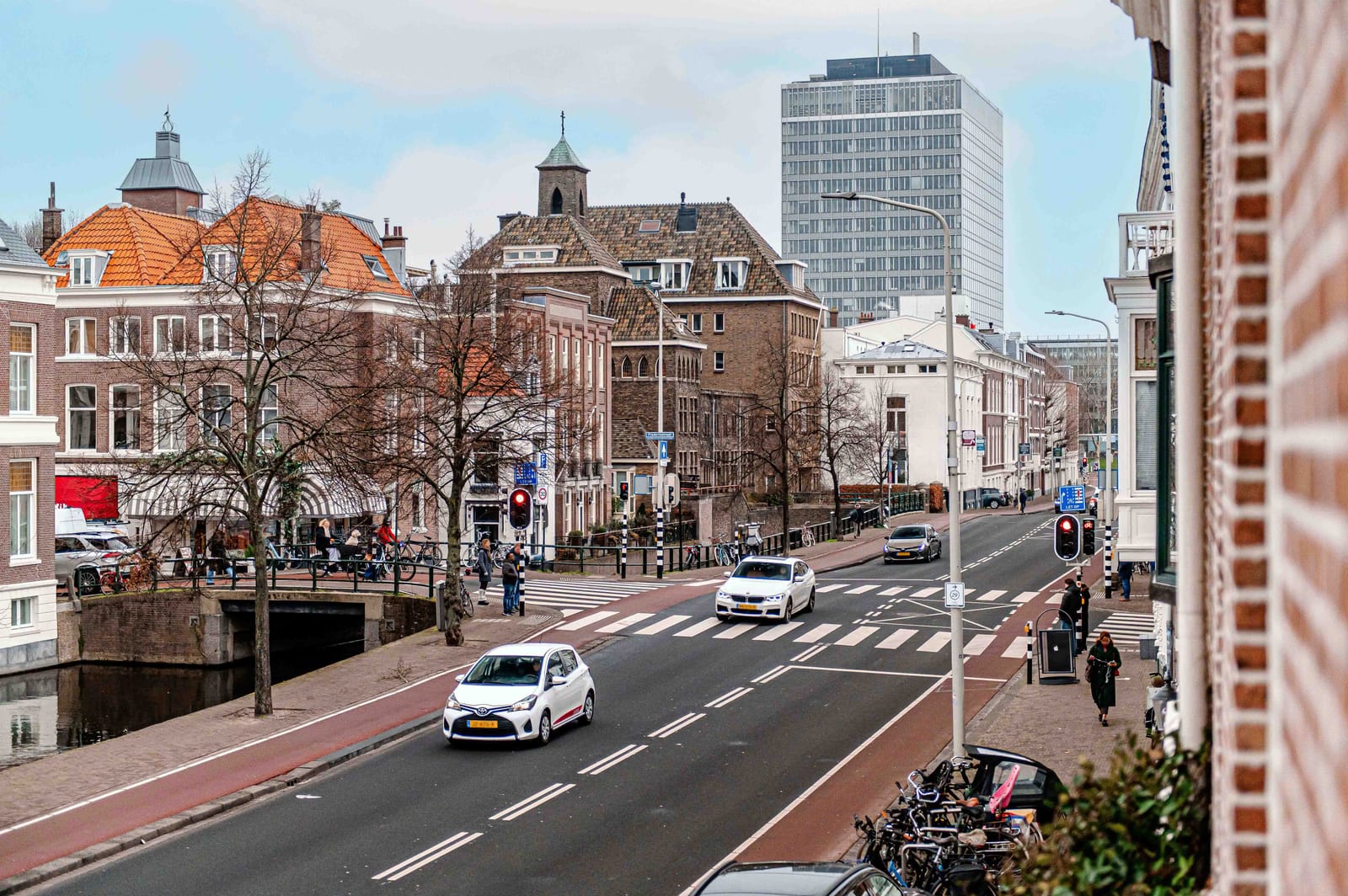 Straatbeeld met de gevel van een woning, geparkeerde auto's en een bewolkte lucht