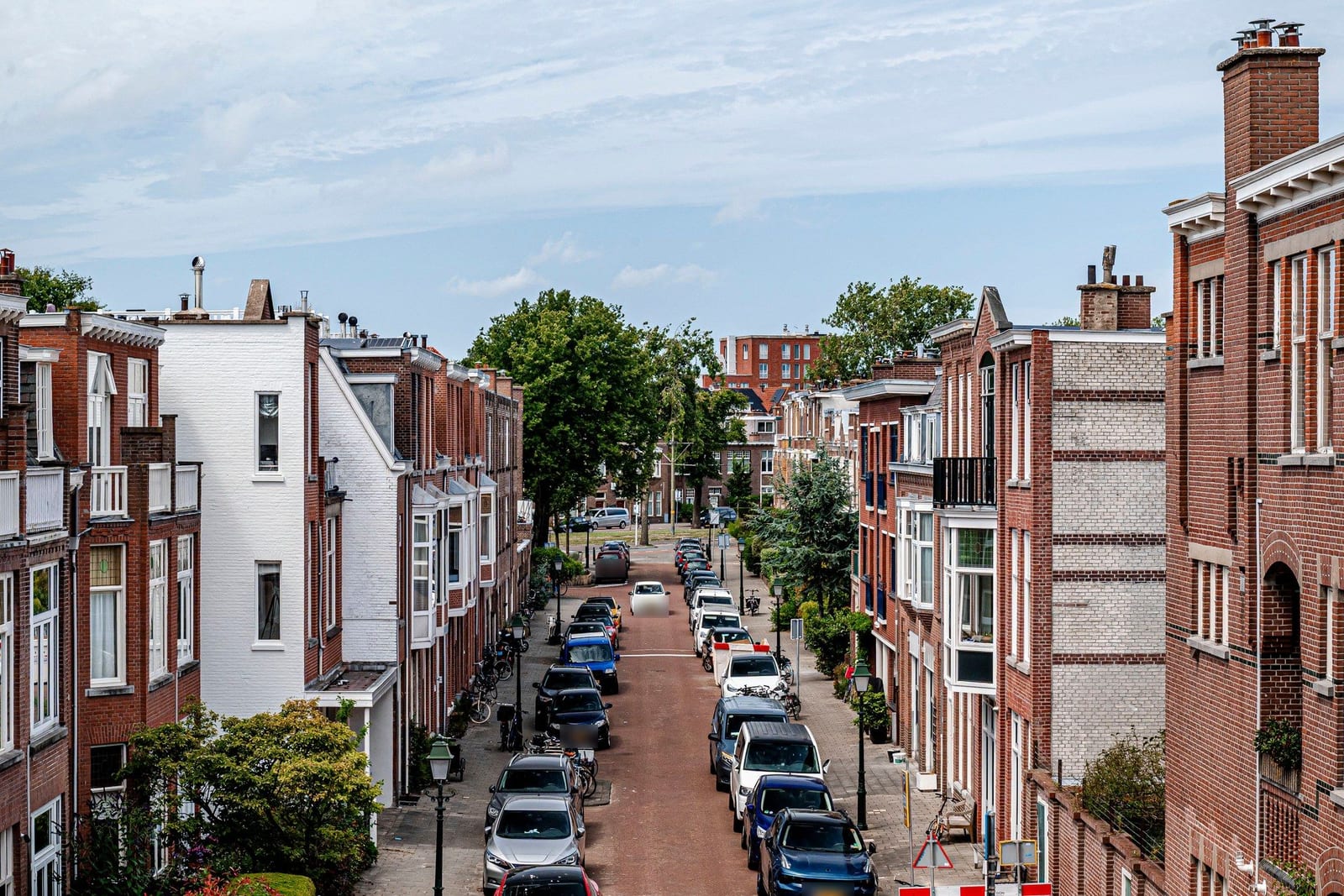Voor: Een straat met bakstenen woningen, geparkeerde auto's en fietsen bij daglicht, en dezelfde straat in de schemering zonder auto's en fietsen, met licht achter de ramen